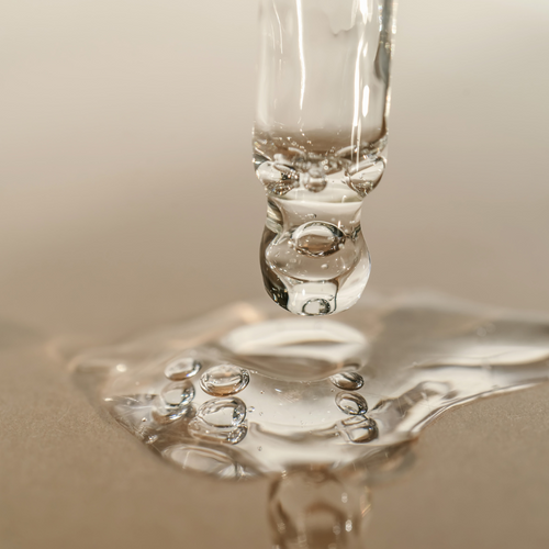 Close-up of a glass dropper with serum dripping onto a surface.