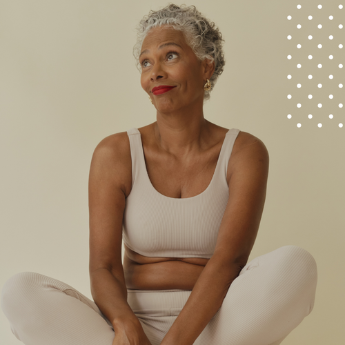 Woman in a beige tank top and white pants sitting against a beige background